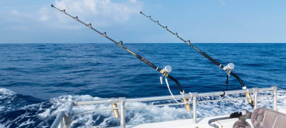 Sport fishing with two salt water rods and reels. Deep sea fishing in the ocean on a sunny blue sky day with fluffy clouds.